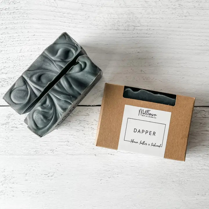 Two bars of soap and a box labeled 'Dapper' on a light wooden surface.
