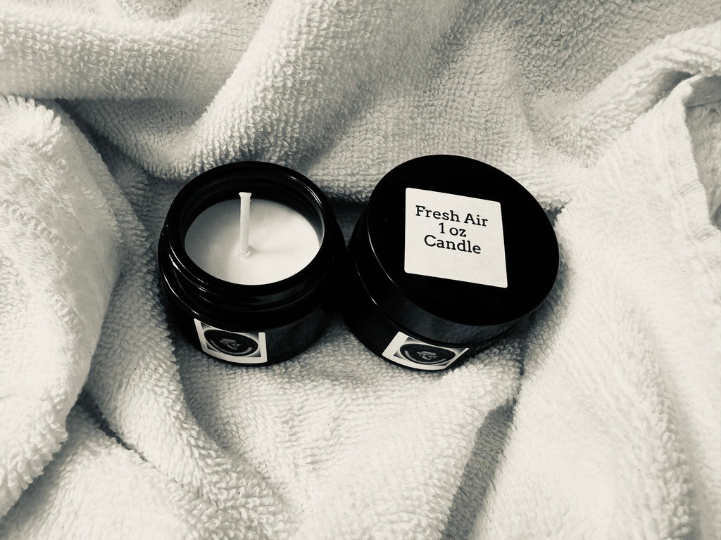 Small candle in a black container with a label on a textured white fabric background