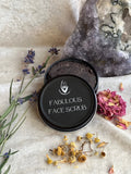 Facial scrub container labeled 'Fabulous Face Scrub' with lavender and flowers on a textured surface.
