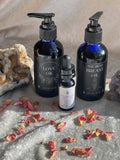Three bottles of oils labeled 'Love Oil', 'The Best Breast Oil', and a smaller dropper bottle on a textured surface with dried flowers.