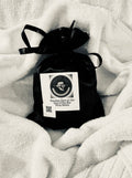 Black wax melt bag with a label on a white blanket velvet bloom beauty and wellness