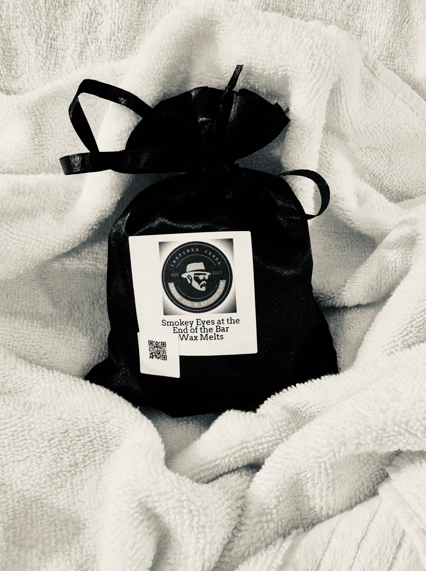 Black wax melt bag with a label on a white blanket velvet bloom beauty and wellness